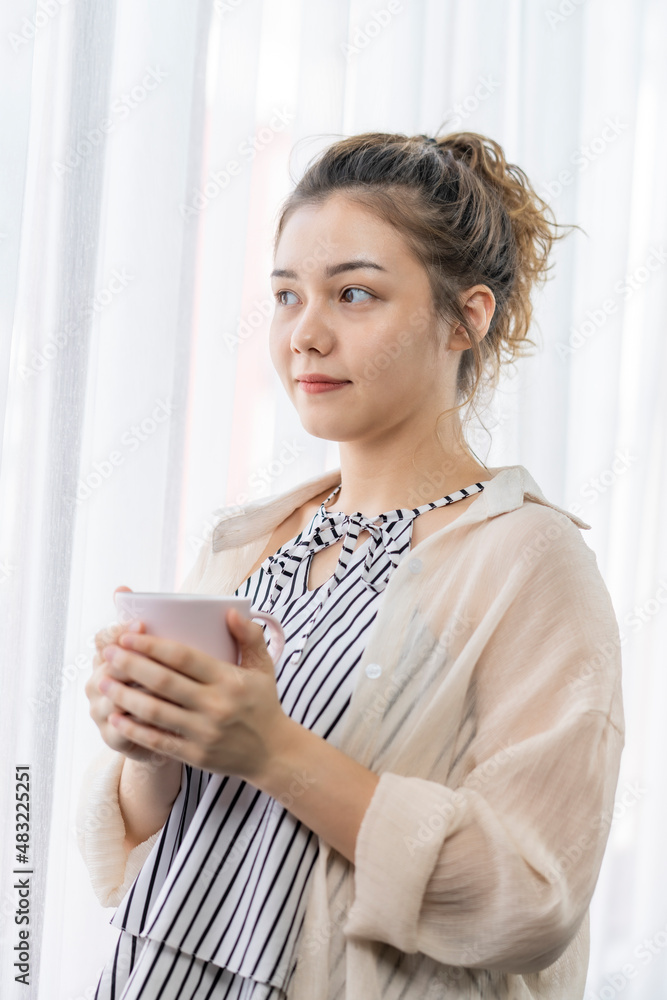 A woman is sitting in front of the window with a cup in her hand. A woman is sitting in front of the window with a cup in her hand.