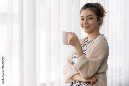 A woman is sitting in front of the window with a cup in her hand.