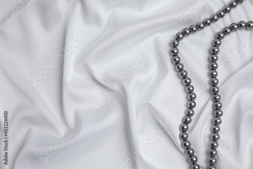 Beautiful pearls on white silk, top view. Space for text