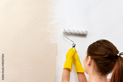 home repairs. painting walls with paint. renovation.
girl child in yellow gloves paints a wall with a roller with white paint.
