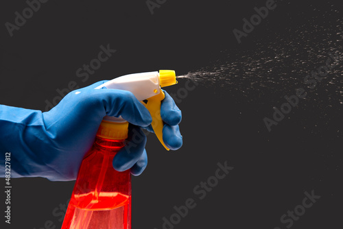 water sprayer bottle in a hand in a protective glove spraying liquid on a dark background. household items for home