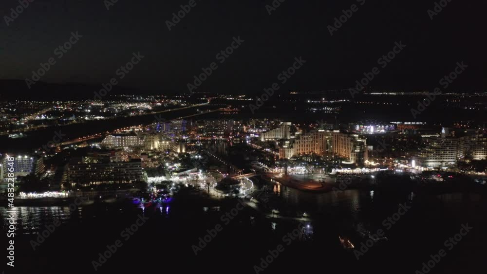 High touristic area with multiple lighted hotels and luminous apartments at the calm Gulf of Eilat during night time. Backwards drone dolly shot High touristic area with multiple lighted hotels and luminous apartments at the calm Gulf of Eilat during night time. Backwards drone dolly shot