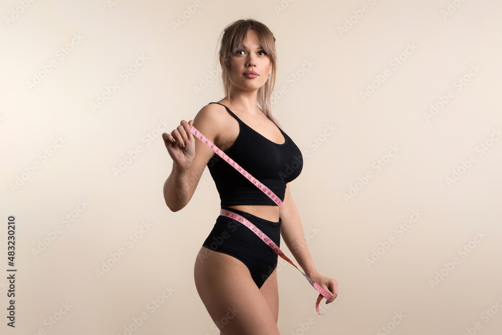 Slim healthy girl in black underwear with measuring tape at waist