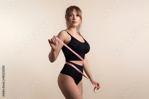 Slim healthy girl in black underwear with measuring tape at waist. Fit Woman poses in high waist panties and top. Perfect female body. Fitness, Diet or body care concept. Female shows her flat belly