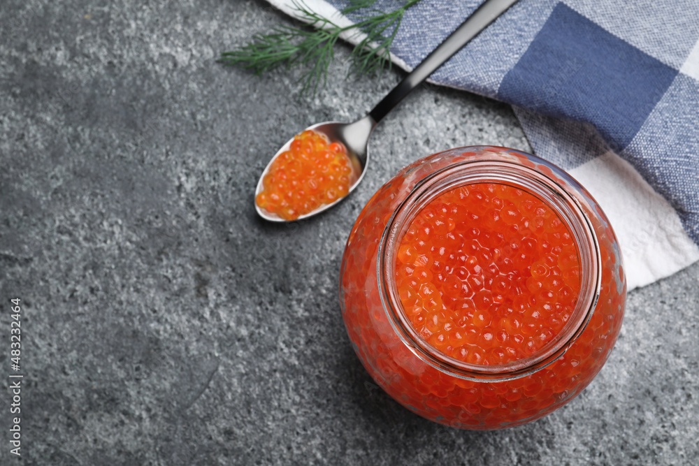 Glass jar and spoon with delicious red caviar on grey table, flat lay. Space for text Glass jar and spoon with delicious red caviar on grey table, flat lay. Space for text