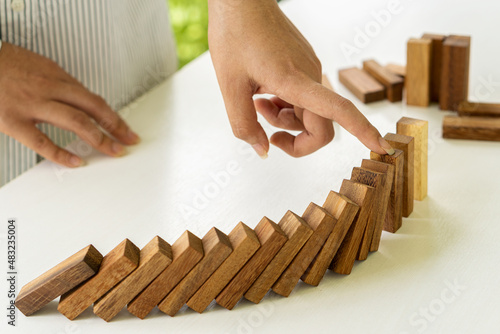 Businesswoman protecting a falling wooden block Business risk planning and strategy selection and hand insurance protection, stop domino, continually topple business risk control concept.