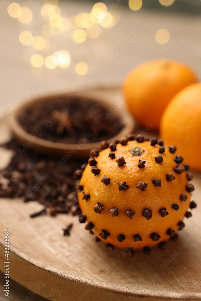 Pomander ball made of tangerine with cloves on wooden table against blurred festive lights, closeup