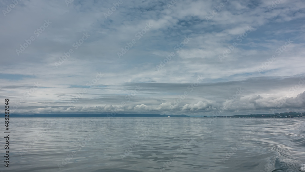 Ripples are visible on the shiny surface of the Pacific Ocean. On the horizon - a mountain range and a lonely ship. Picturesque clouds in the sky. Pastel shades of blue. Kamchatka. Avacha Bay