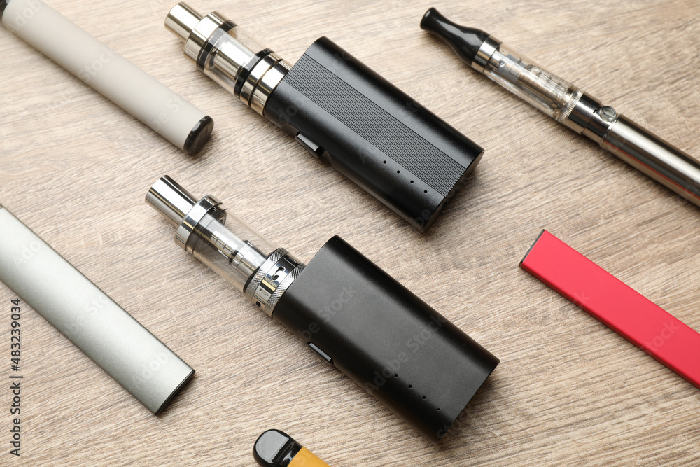 Different electronic cigarettes on wooden table, flat lay. Smoking alternative Different electronic cigarettes on wooden table, flat lay. Smoking alternative