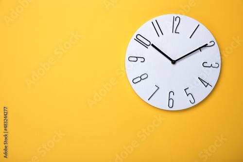 Modern clock on yellow background, top view. Space for text