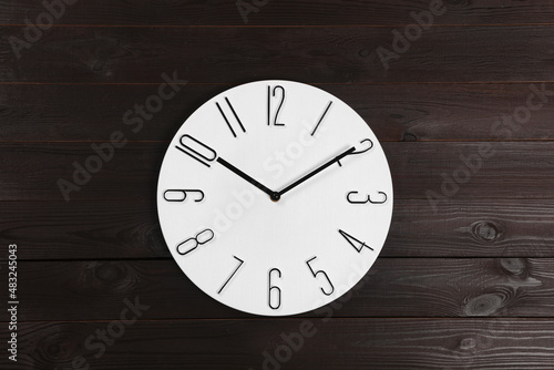 Stylish analog clock hanging on wooden wall
