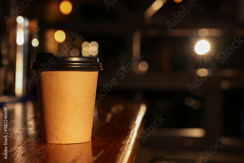 Paper coffee cup on wooden table in cafe. Space for text