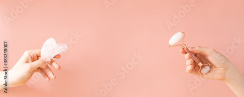 Fototapeta Naklejka Na Ścianę i Meble -  Female hands holding a gua sha facial roller and a massage jade stone, on a beige background. Skin care procedures, a place to copy