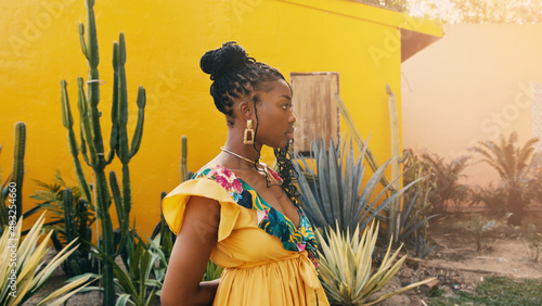 portrait of a beautiful African-American woman with cactuses by a yellow wall in the background. ethno concept photo