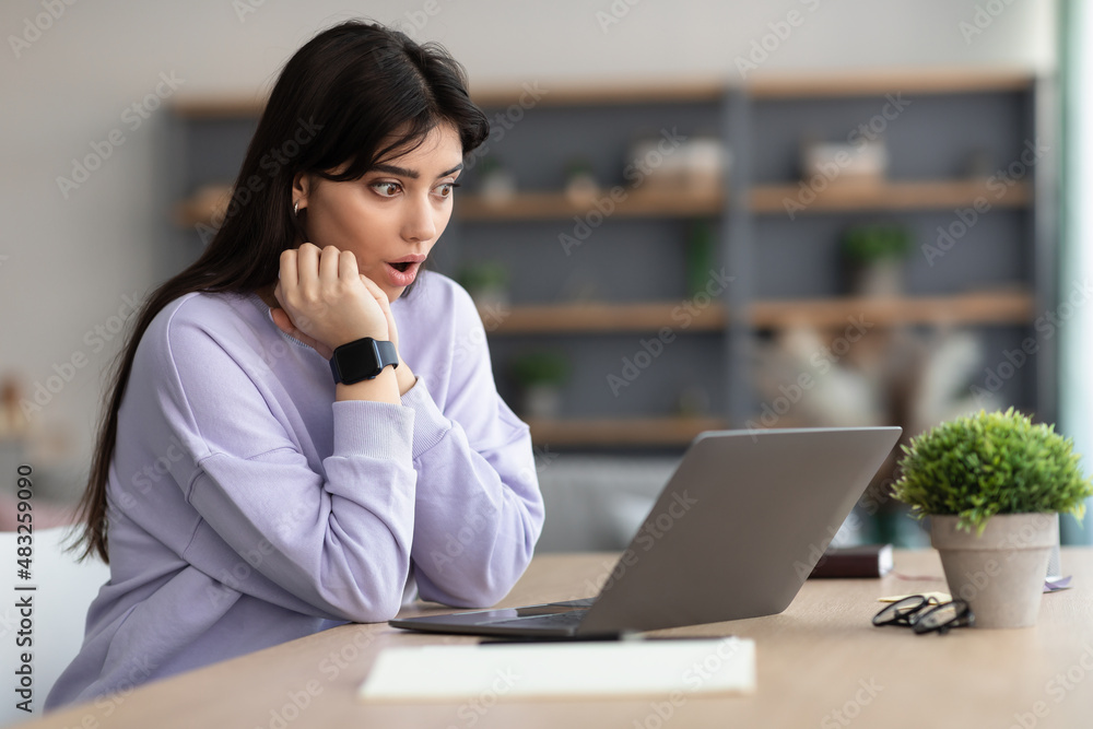 Surprised woman sitting at desk, using laptop Surprised woman sitting at desk, using laptop