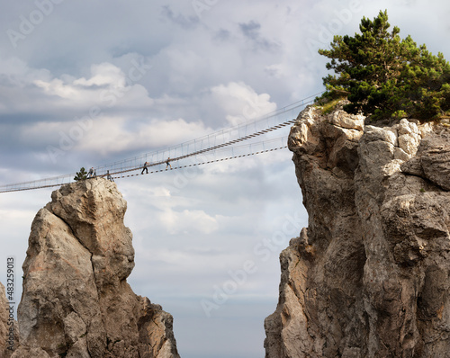 Suspension bridge between the rocks. Air mountain road, tourists. Photo.