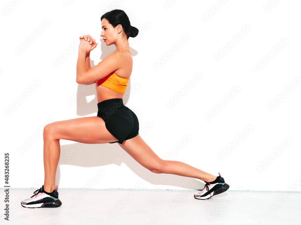 Obraz premium Portrait of fitness confident woman in black sports clothing. Sexy young beautiful model with perfect body. Female isolated on white wall in studio. Stretching out before training. Doing lunges