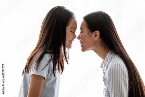 Loving asian mom and daughter touching each other with noses over white background, side view