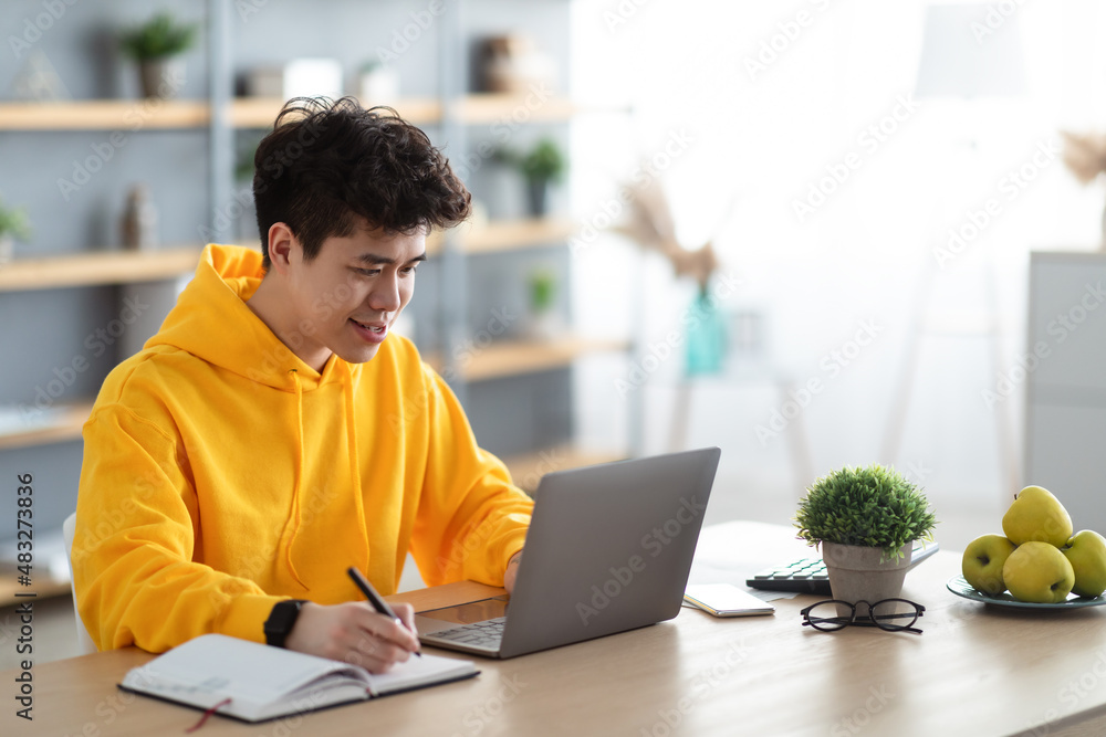 Smiling asian man working on laptop and writing Smiling asian man working on laptop and writing