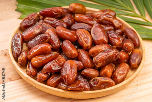Dried date palm fruit on a wooden plate, date palm fruit with leaf on wooden background