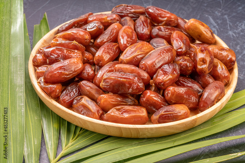 Dried date palm fruit on a wooden plate, date palm fruit with leaf on wooden background