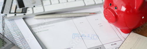 Invoice with paid stamp with bank cards and piggy bank on table