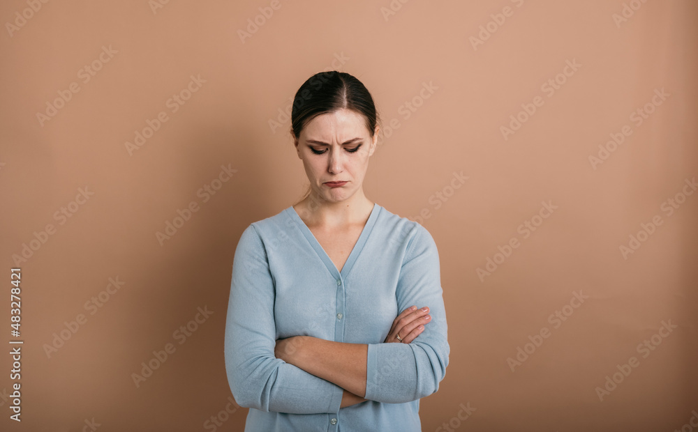 Obraz premium a disgruntled brunette woman with glasses in a blue jumper stands and lowered her eyes down on a beige background with a place for text
