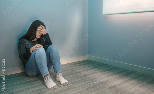 Depressed woman overwhelmed by pandemic fatigue sitting on the floor with hand on head