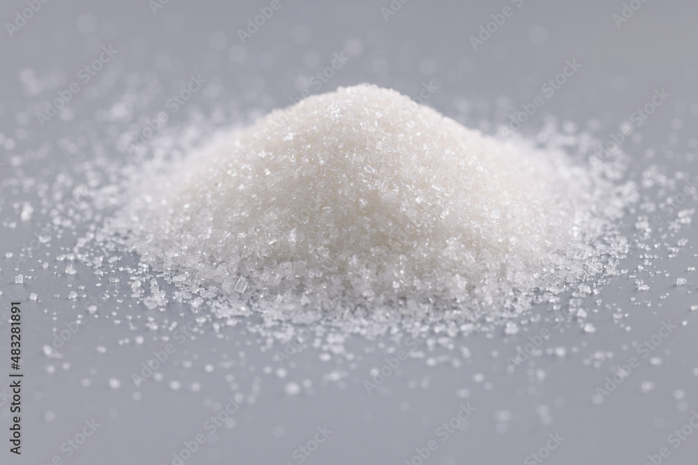 Pile of sugar crystals on grey surface, focus on heap of sweet powder to add in dishes