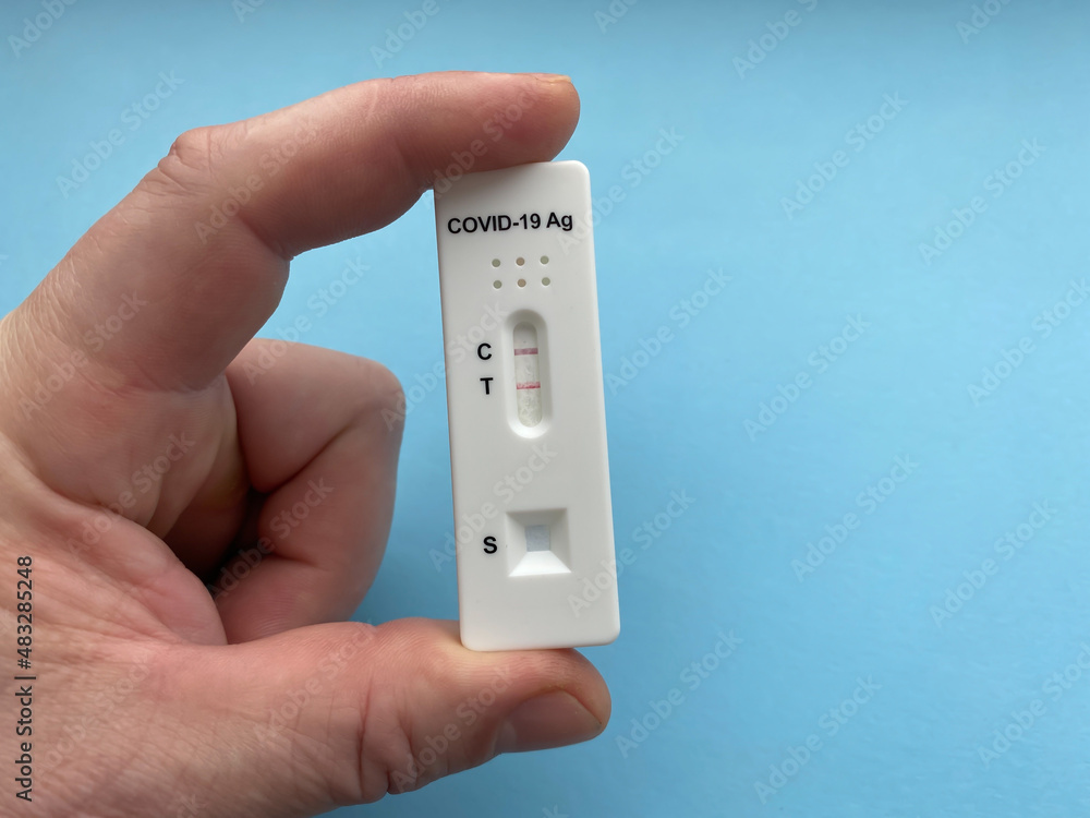 Positive rapid test result for Covid-19. Coronavirus (sars-CoV-2) rapid antigen detection device in hand close-up. Isolate On a blue background. Positive rapid test result for Covid-19. Coronavirus (sars-CoV-2) rapid antigen detection device in hand close-up. Isolate On a blue background.