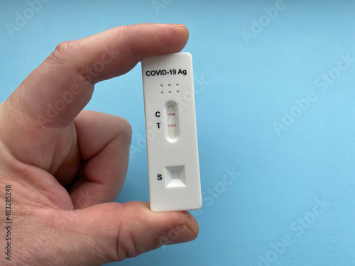 Positive rapid test result for Covid-19. Coronavirus (sars-CoV-2) rapid antigen detection device in hand close-up.  Isolate On a blue background.