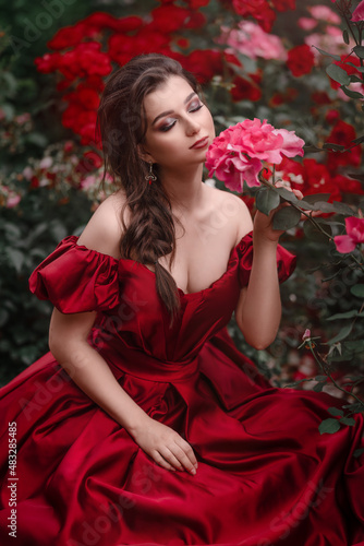 Beautiful woman in red dress walking in the garden full of roses.