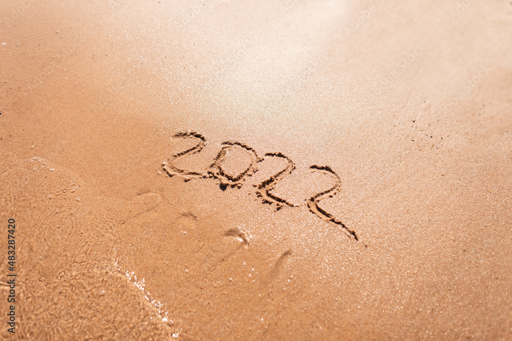 Fototapeta premium 2022 years and 2021 washed away by a wave on the sand. New year 2022 concept. Summer vacation and travel by sea