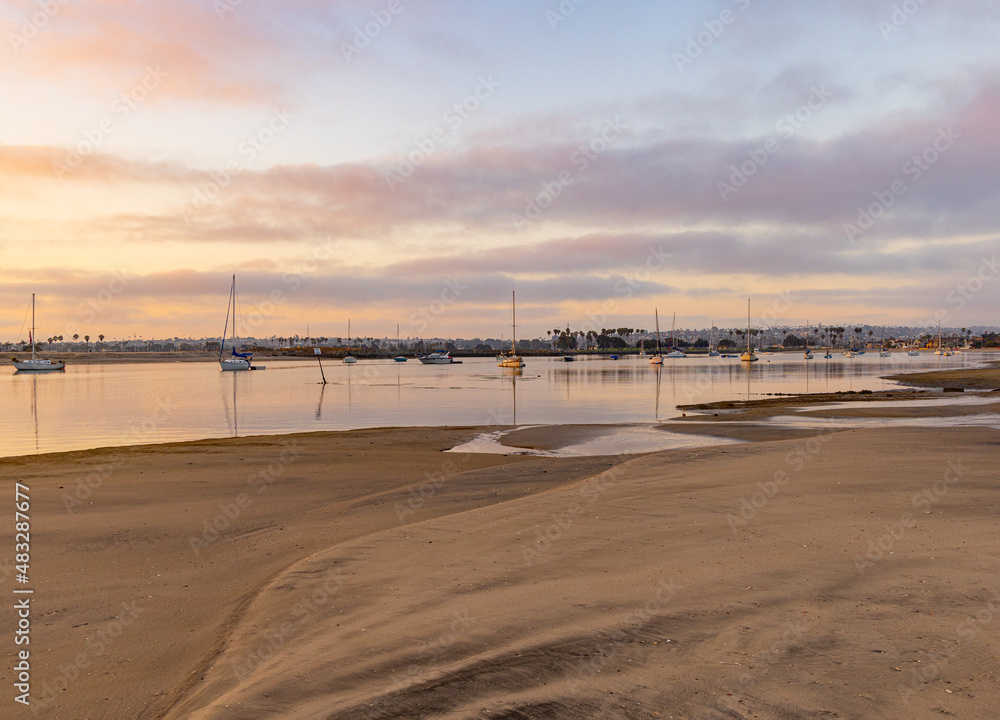 Sunrise on the Mission Bay in California shows boats with their reflections in the orange of the rising sun. Sailors ready to take their sailboats on an adventure
