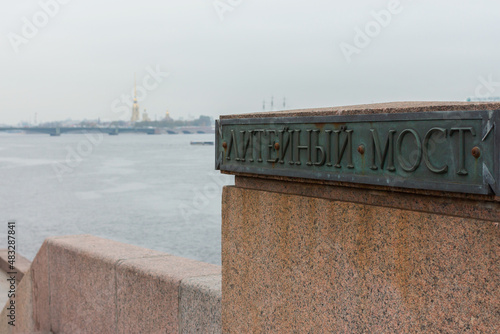 Canvas Print Close-up view of parapet fragment with name of Liteyny Bridge at cold cloudy day, defosused Neva panorama at background