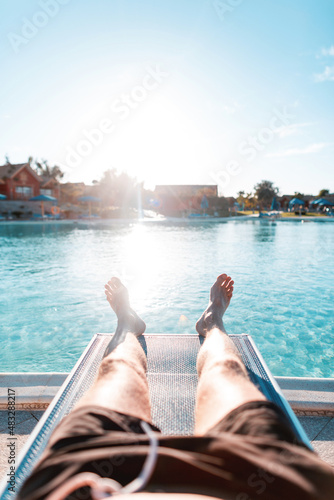 Billede på lærred Young man rest on a beach lounger near swimming pool with blue water at sunset