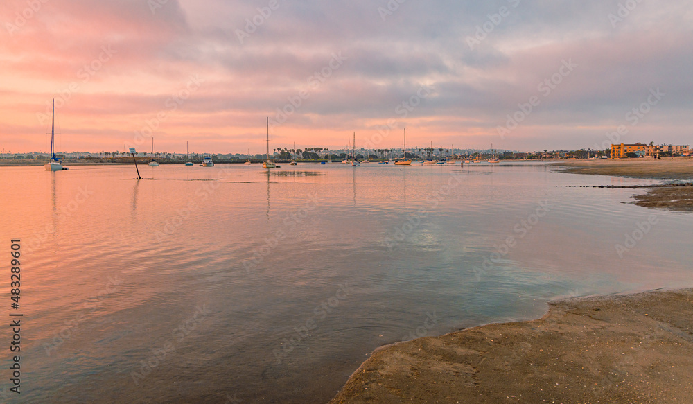 Sunrise on the Mission Bay in California shows boats with their reflections in the orange of the rising sun. Sailors ready to take their sailboats on an adventure