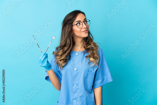 Woman dentist holding tools over isolated on blue background thinking an idea while looking up