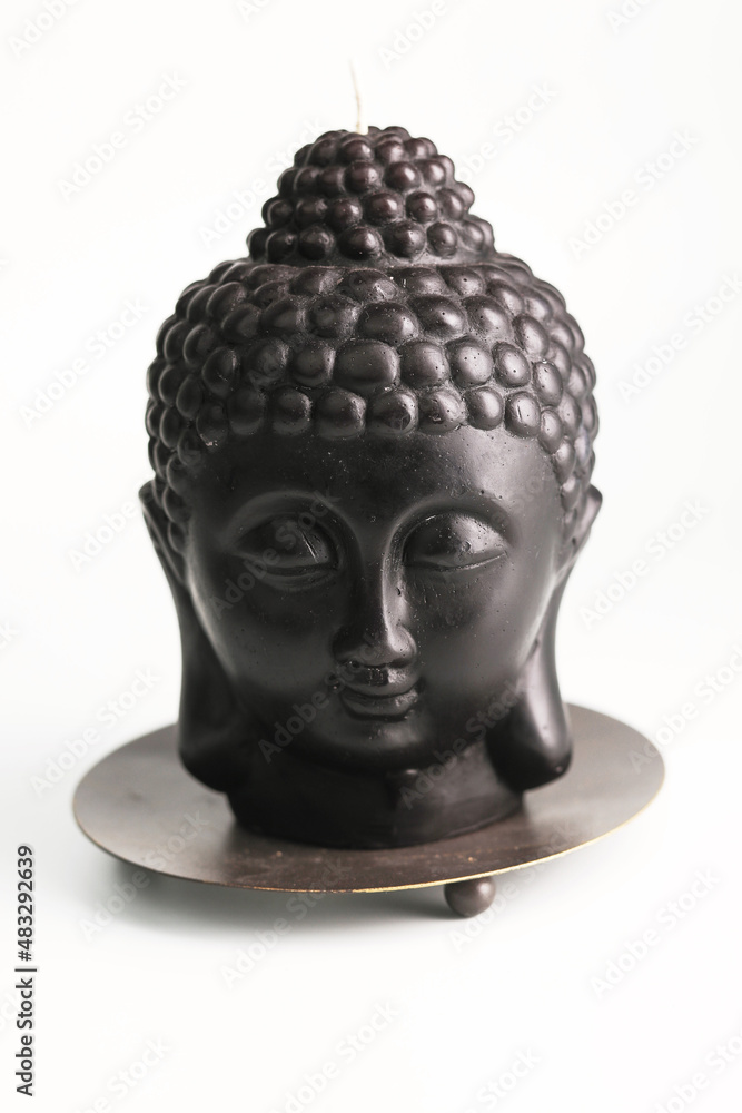 A brown candle in the shape of Buddha's head, used for meditation and relaxation in buddhist religion, white background