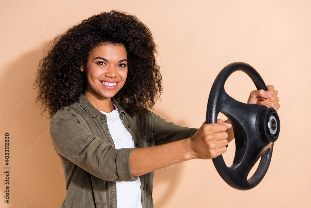 Portrait of attractive cheerful girl holding steering wheel taxi service isolated over beige pastel color background Portrait of attractive cheerful girl holding steering wheel taxi service isolated over beige pastel color background