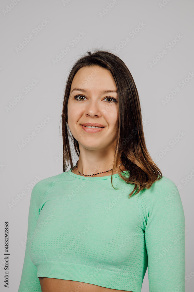 Beautiful woman posing in studio. Portrait of happy young brunette in green top for yoga or fitness, she stands on gray isolated background and smiles. Beautiful woman posing in studio. Portrait of happy young brunette in green top for yoga or fitness, she stands on gray isolated background and smiles.