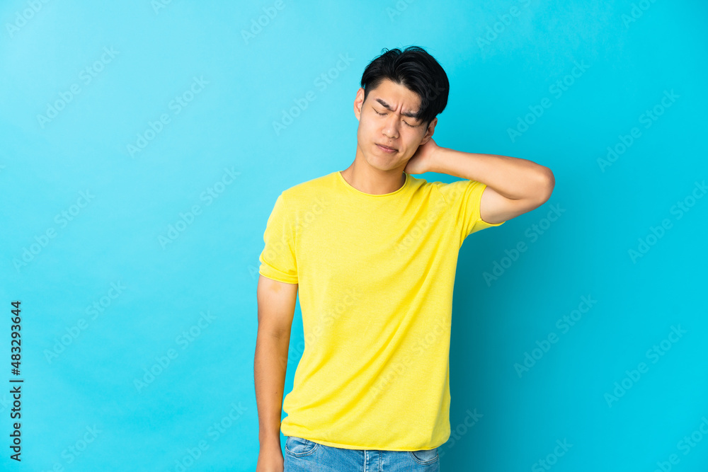 Young Chinese man isolated on blue background with neckache Young Chinese man isolated on blue background with neckache