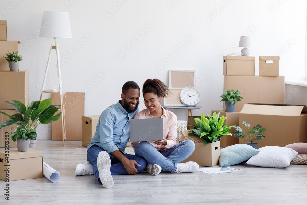 Glad young african american family resting, sitting on floor among cardboard boxes with things Glad young african american family resting, sitting on floor among cardboard boxes with things