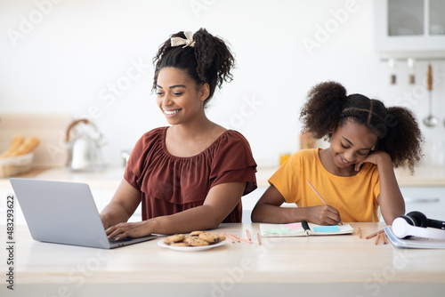 School girl doing homework by her working mother, kitchen interior