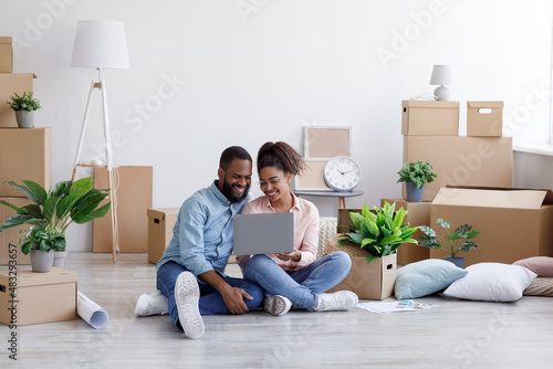 Glad young african american family resting, sitting on floor among cardboard boxes with things