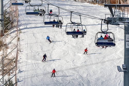 Fotografie People sitting on chairlift and skiers skiing downhill on slope at mountain resort