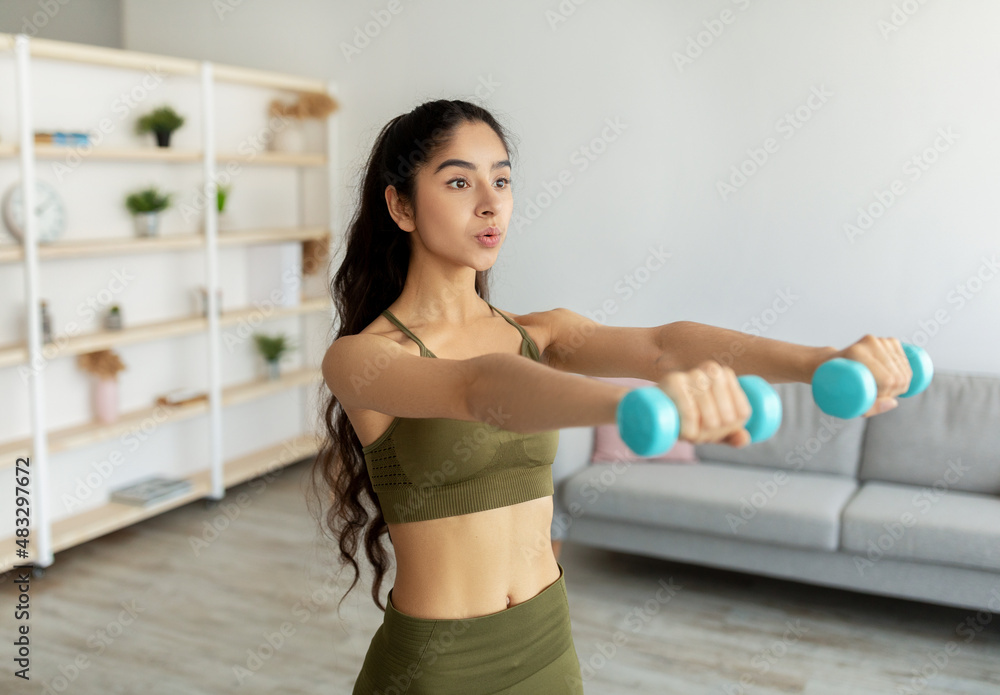 Domestic sports during covid lockdown. Strong Indian woman doing exercises with weights, working out with dumbbells Domestic sports during covid lockdown. Strong Indian woman doing exercises with weights, working out with dumbbells