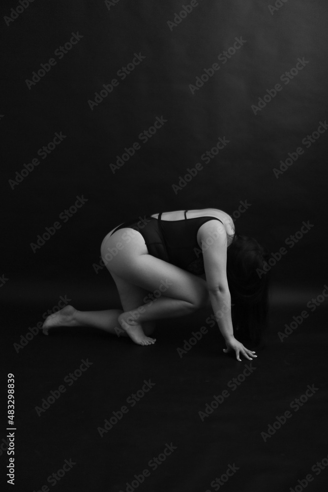 A brunette girl with curvaceous poses in a black classic bodysuit on a black background.  body abstraction on black background