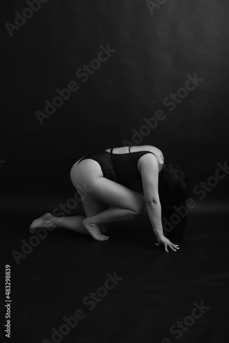 A brunette girl with curvaceous poses in a black classic bodysuit on a black background. body abstraction on black background