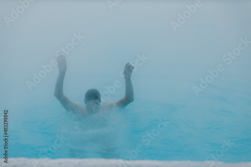 Fit swimmer male training swim in open winter swimming pool with fog. Geothermal outdoor spa health concept, photo